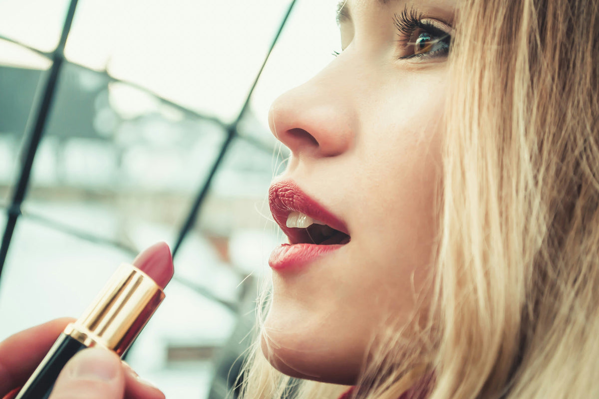 Woman applying Revlon Super Lustrous Lipstick in a bold red-pink shade