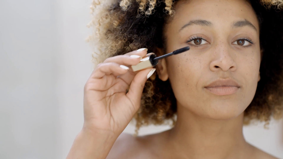 Woman applying black mascara to eyelashes with wand close-up